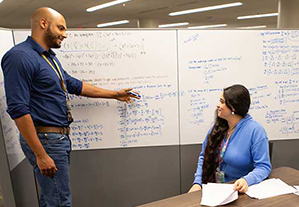 ACS tutor is explaing a topic on a white board to two students.